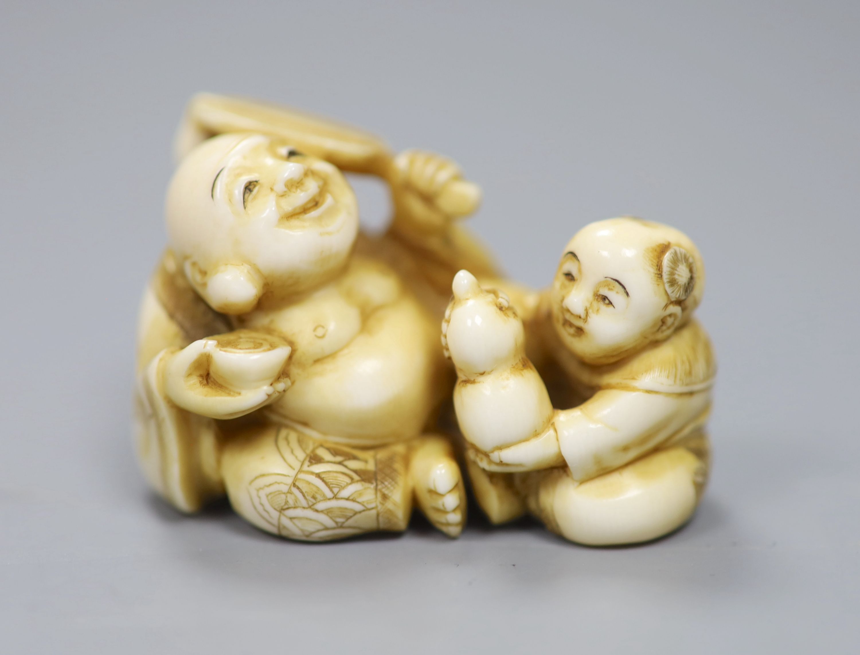 A Japanese ivory netsuke in the form of a seated Hotei and attendant, early 20th century 3cm high, 5cm wide, signed to underside, toget